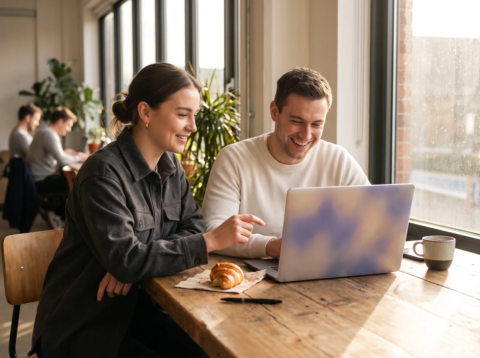Professionals laughing over smartphones and laptop at co-working table